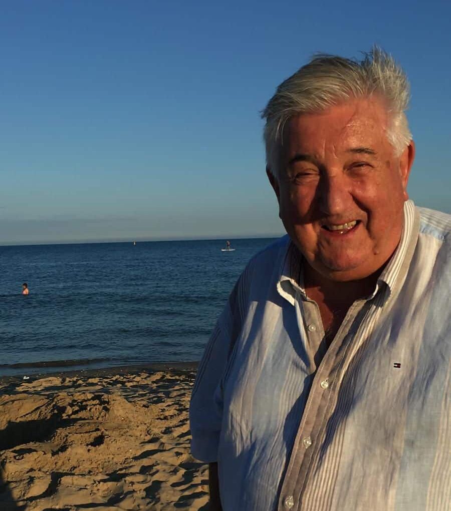 Smiling elderly man standing on a sandy beach with the ocean in the background